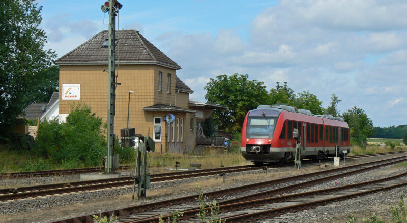 Ein Zug im Bahnhof Neuwittenbek, Blick auf das Empfangsgebäude. Davor drei Gleise, am Bahnsteig ein Zug.